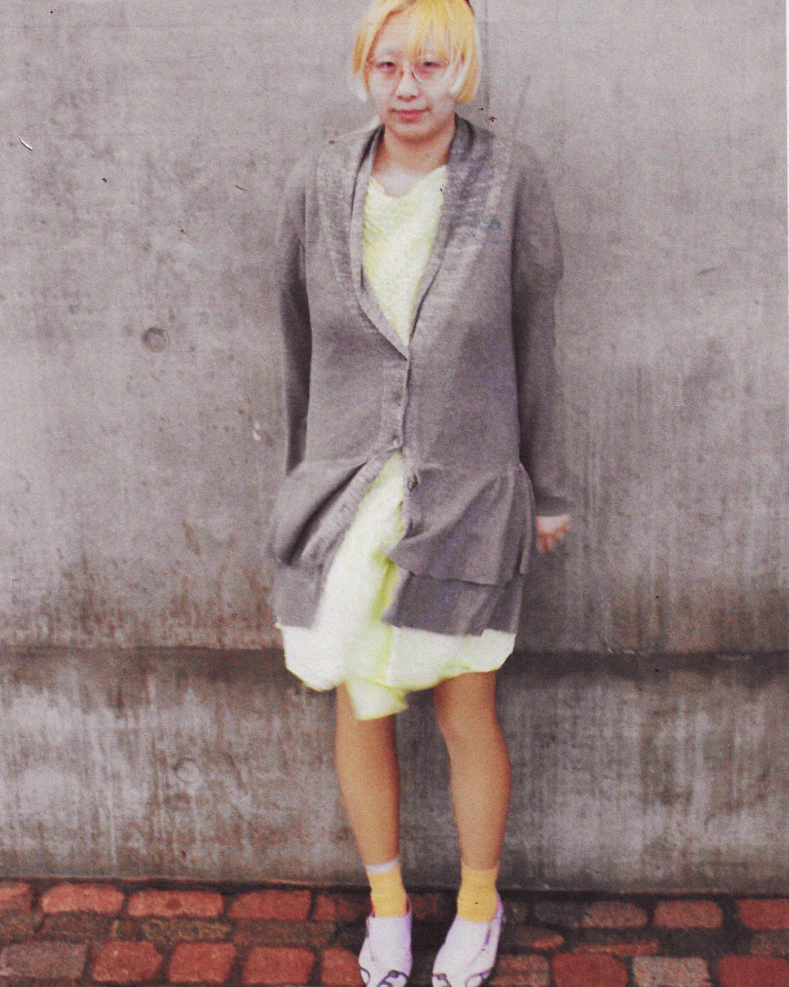 A full length photograph of a woman wearing a grey cardigan and green dress in London.