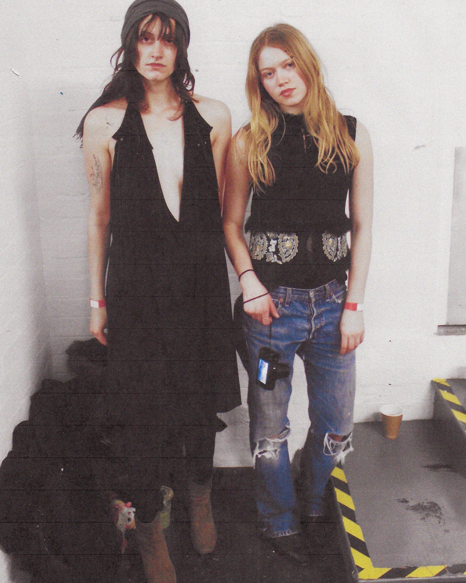 A full length photograph of two women in London, one wearing a black dress, the other a black top and blue jeans.