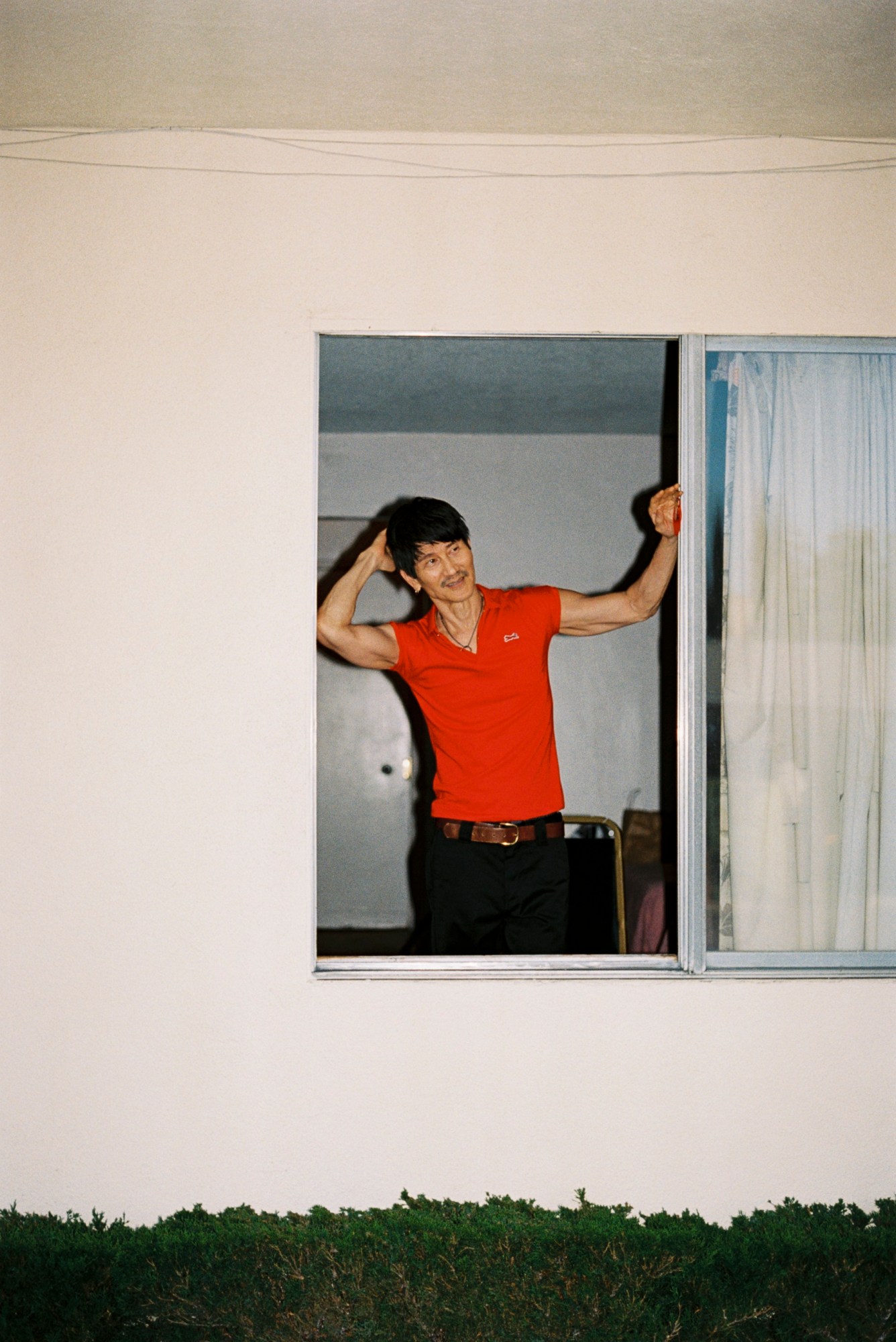 Gregg Araki by Kevin Amato for i-D magazine issue 375, fall/winter 2025. He wears a red polo shirt and is looking through a window pane